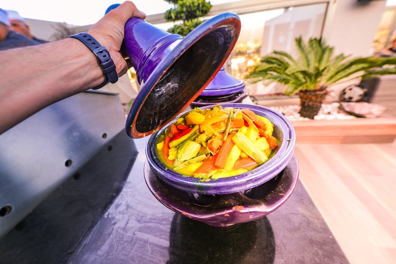 Vibrant vegetable tagine being uncovered in a purple pot. Perfect for food enthusiasts.